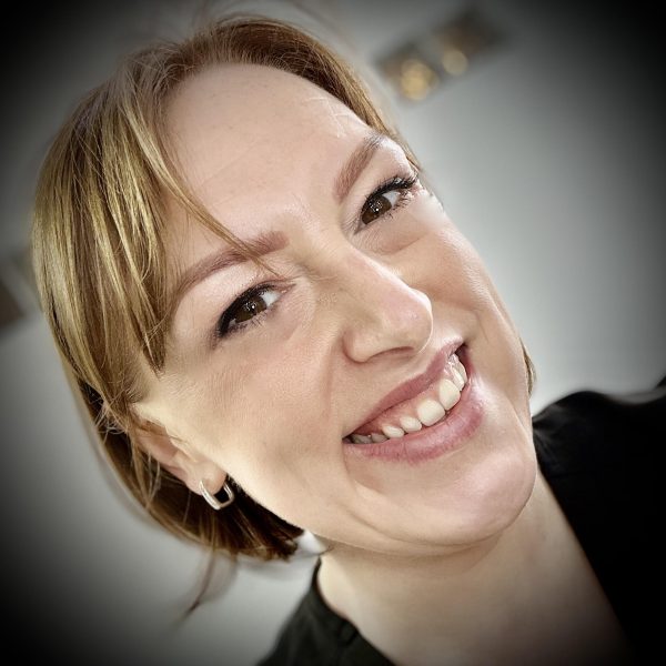 A woman with a tattoo smiling in front of a black background.